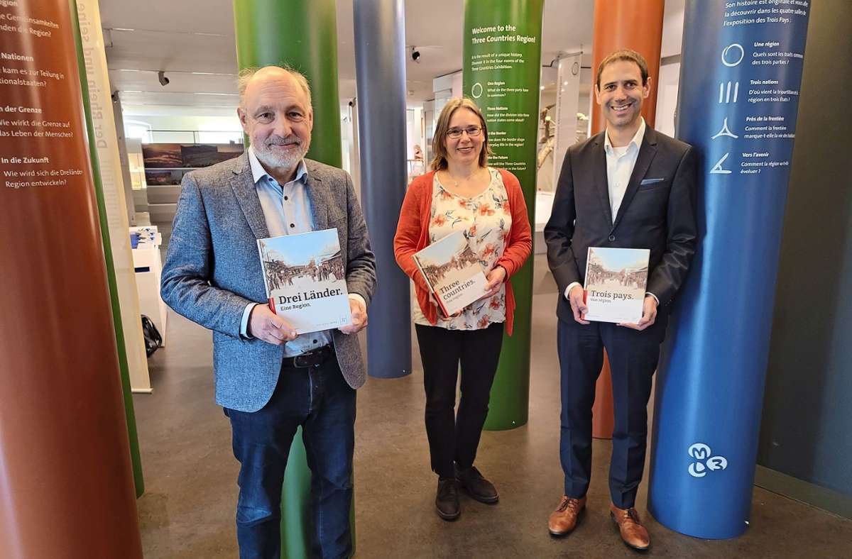 Markus Moehring (v.l.), Birgit Bayerlein und Christian Eschbach präsentieren die drei Sprachversionen des neuen Buchs im Eingangsbereich der Dreiländerausstellung. Foto: Markus Greiß