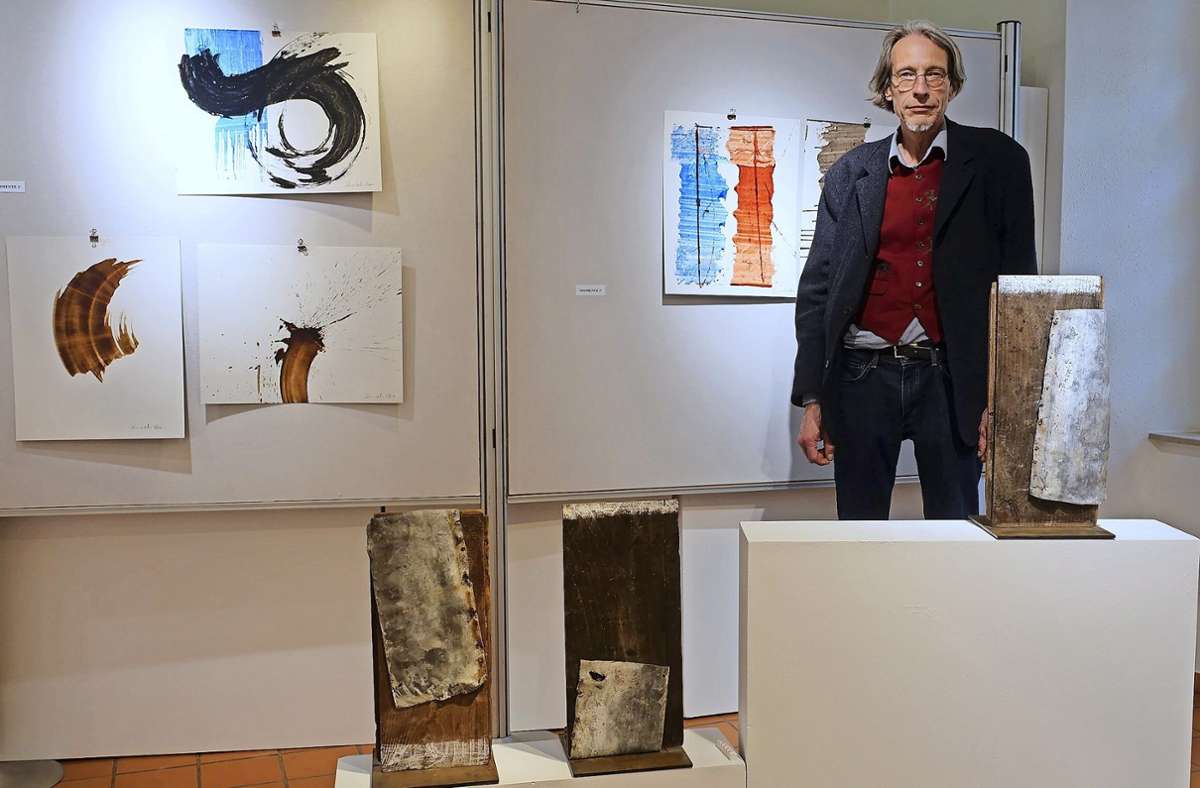 Thomas Oehm neben seinen Metall-Holz-Skulpturen auf Sockeln und den Tintenmalereien. Foto: Jürgen Scharf